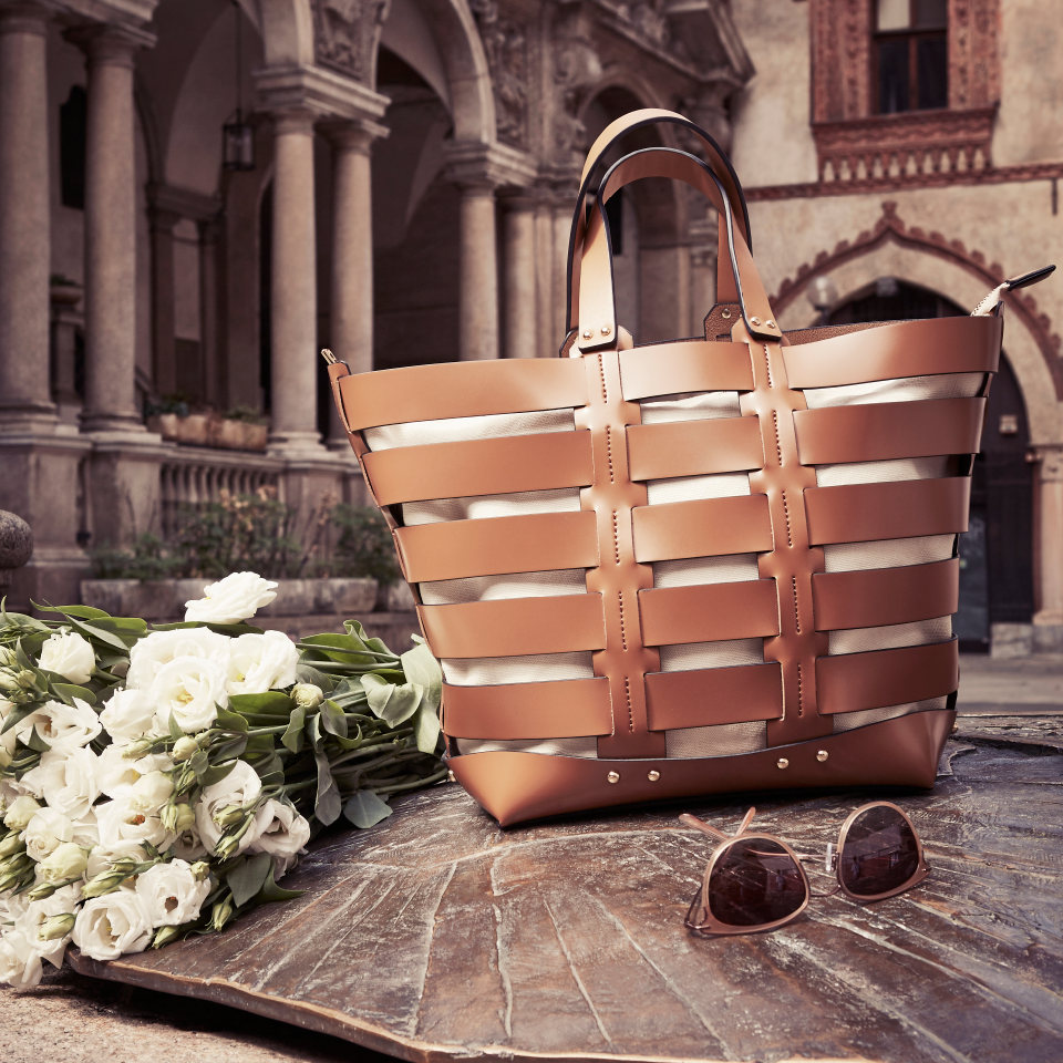 ChatGPT: Braune Handtasche aus Leder auf einem Brunnendeckel in einem Innenhof in Italien. Daneben weiße Blumen und eine Sonnenbrille.