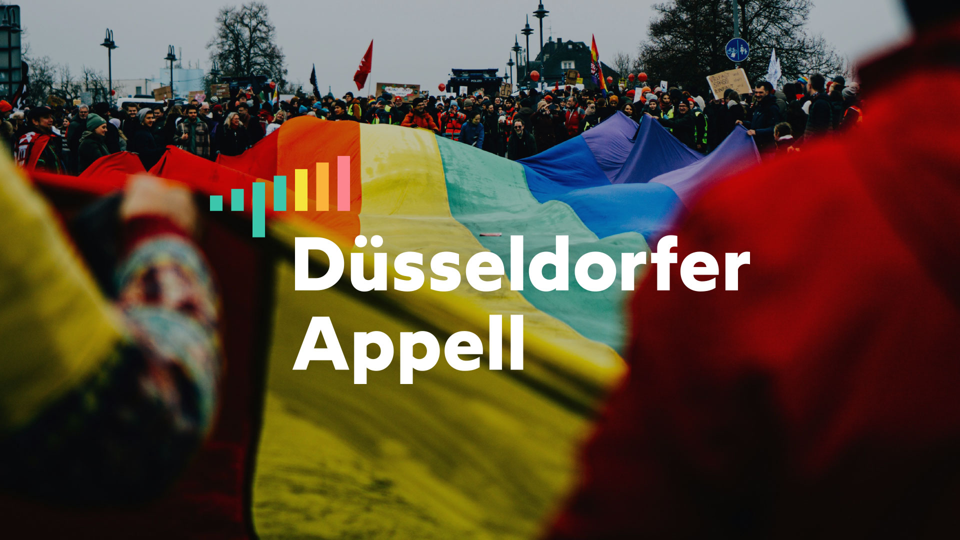 Kundgebung mit großer Regenbogenflagge und Logo des Düsseldorfer Appells für Vielfalt und Demokratie.