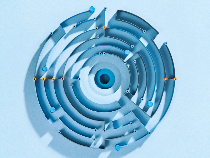 Kreisförmiges, abstraktes Labyrinth aus Papier mit orangenen Highlights auf hellblauem Hintergrund.