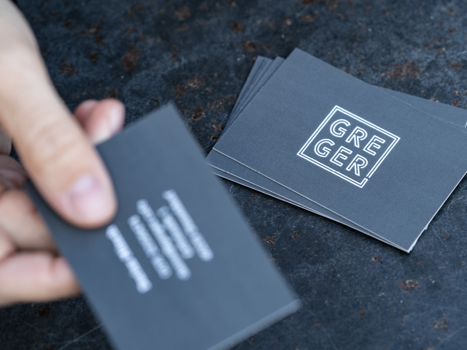 Graue Visitenkarten mit weißem Logo "Greger"