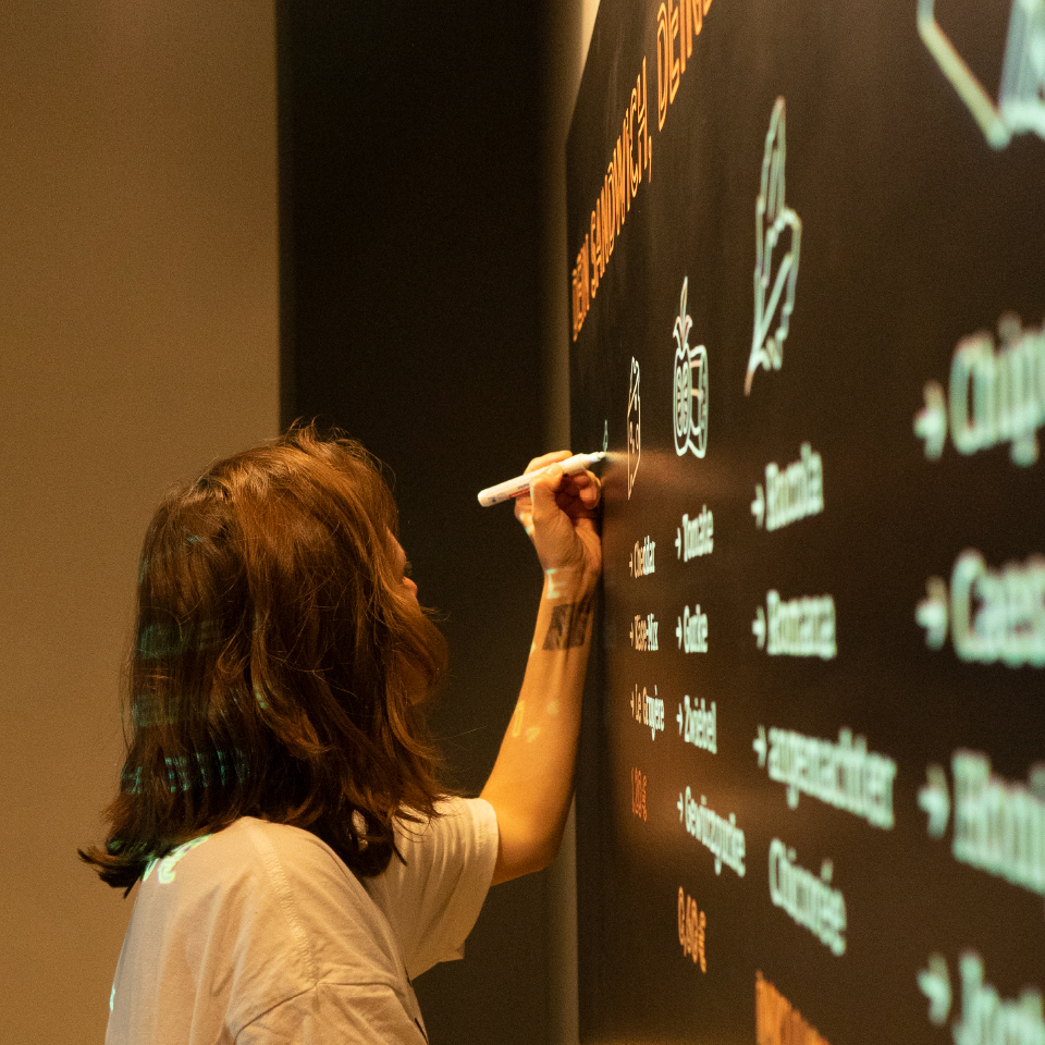 Person beschriftet eine große schwarze Menütafel mit weißen und farbigen Markern.