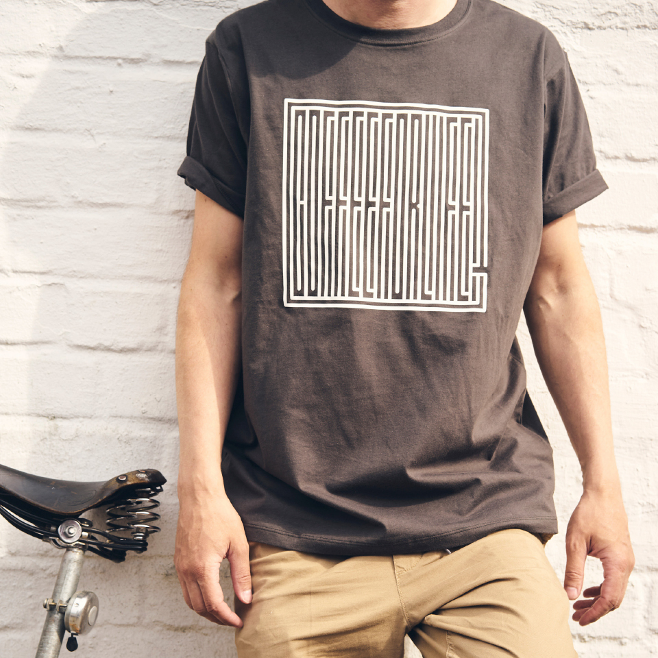 Person in grauem T-Shirt mit "Coffee for life" Aufdruck lehnt an weißer Mauer