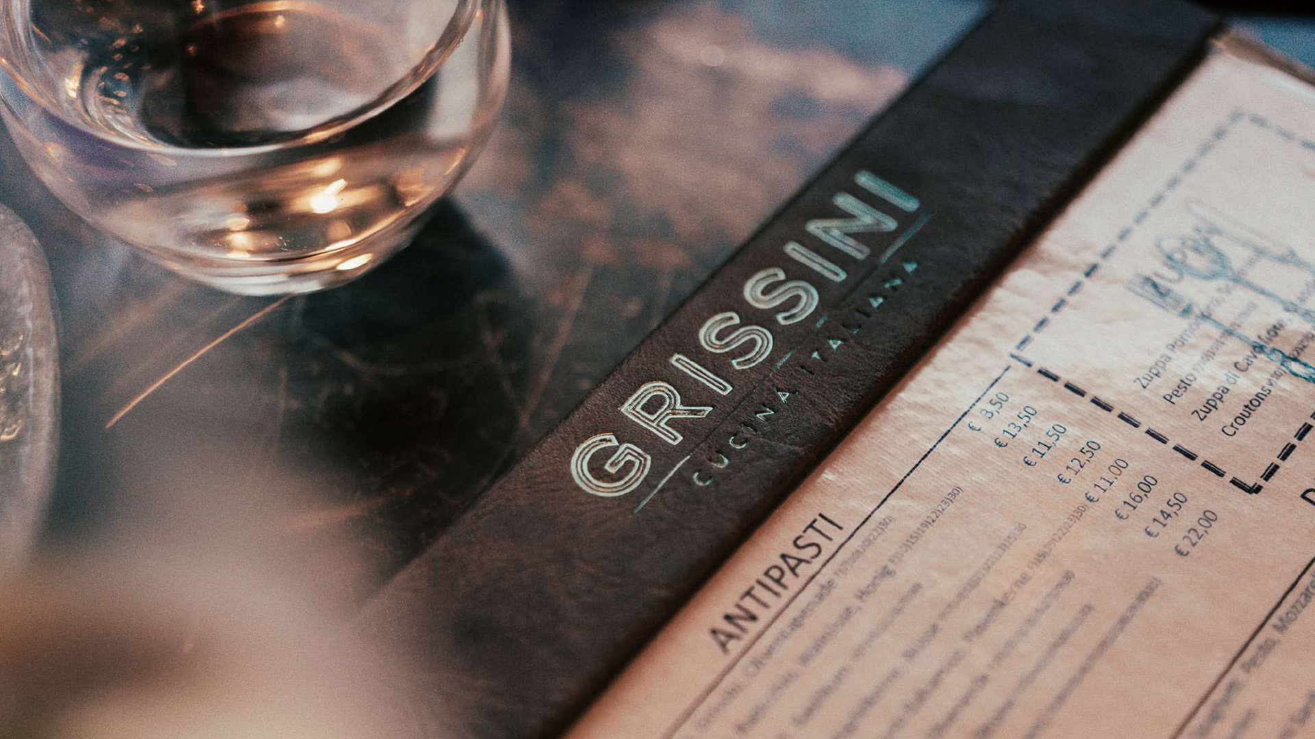 Nahaufnahme einer Restaurantkarte mit dem Logo „Grissini Cucina Italiana“ und Menüausschnitt mit Preisen.