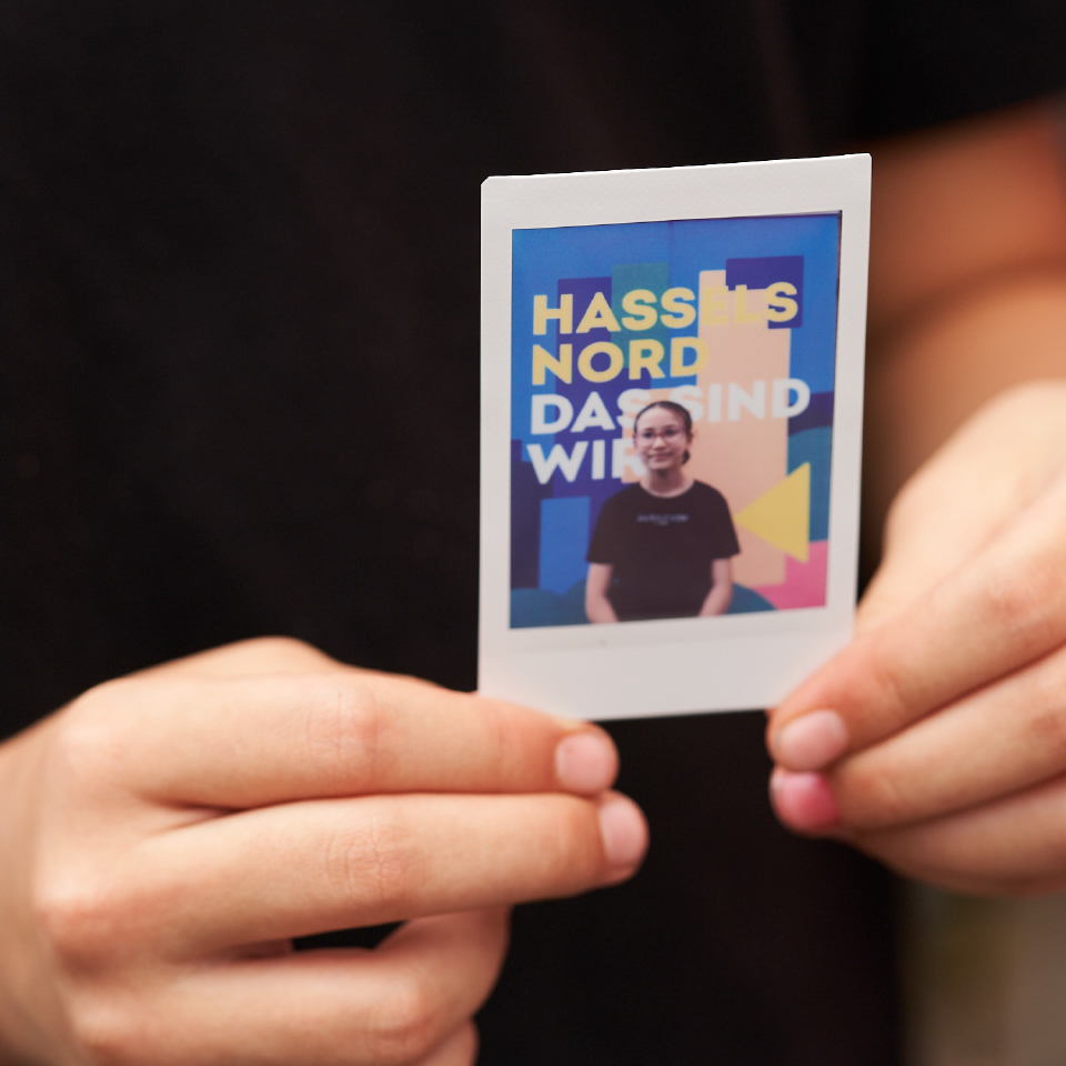 Person hält ein Polaroid mit Portraitfoto und dem Key Visual der Kampagne „Hassels Nord – Das sind wir!“.