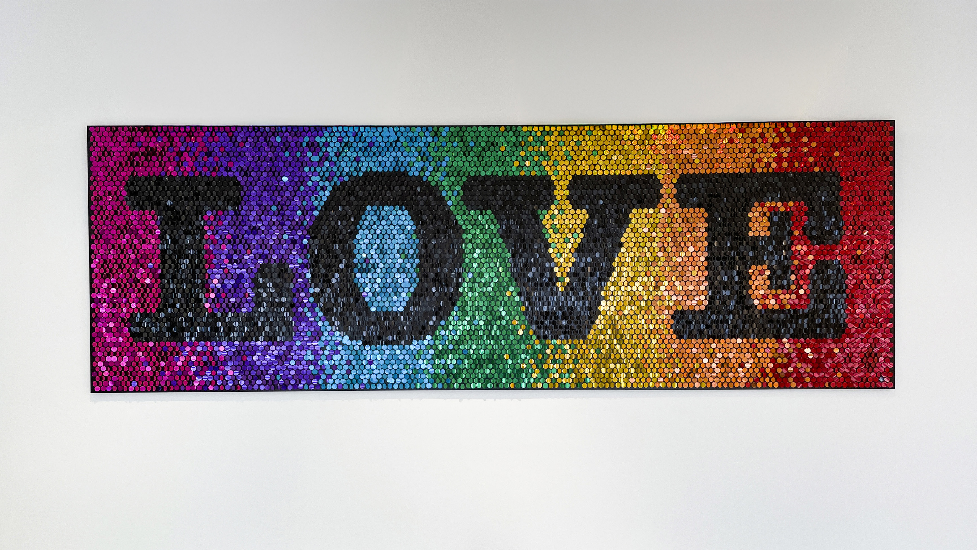 Wandkunstwerk aus Pailletten mit dem Wort „LOVE“ auf regenbogenfarbenem Hintergrund.