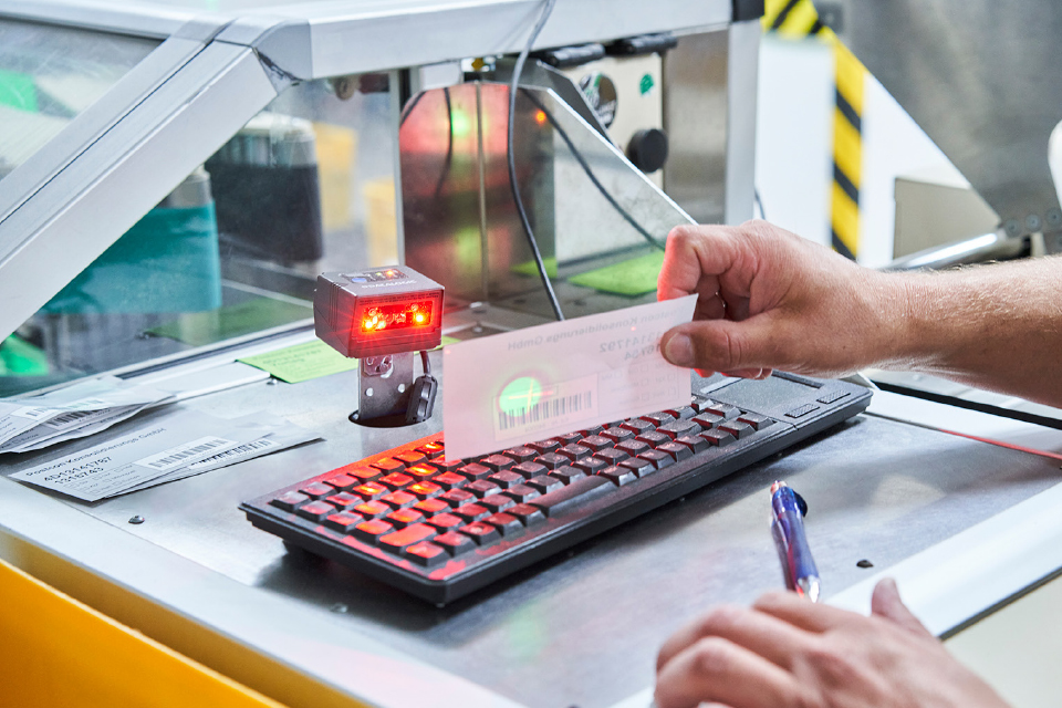 Hand scannt einen Barcode an einem Postcon-Arbeitsplatz.