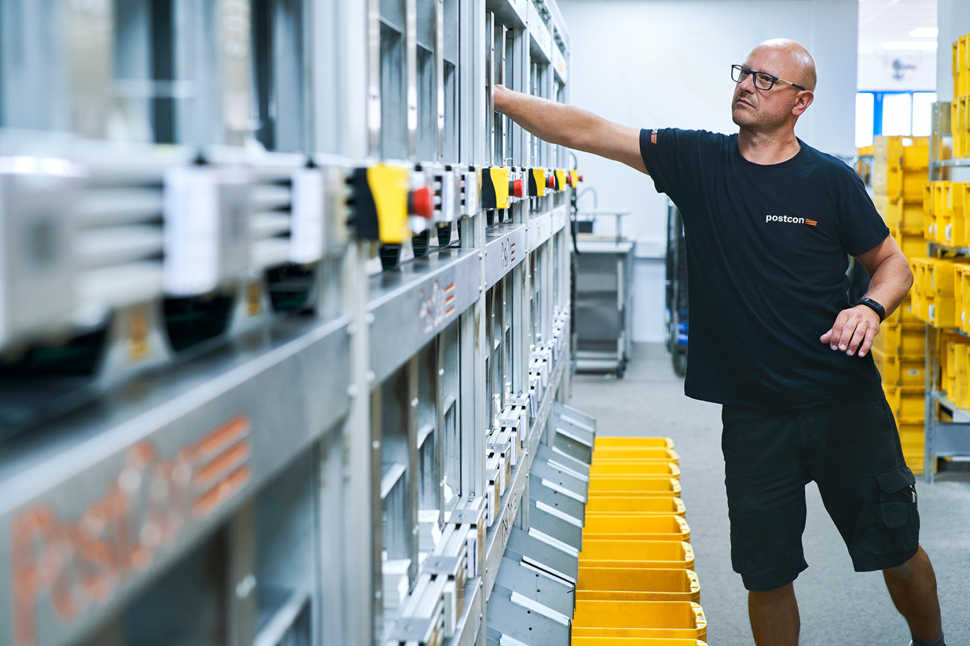 Mitarbeiter von Postcon bedient Sortieranlage mit gelben Behältern.