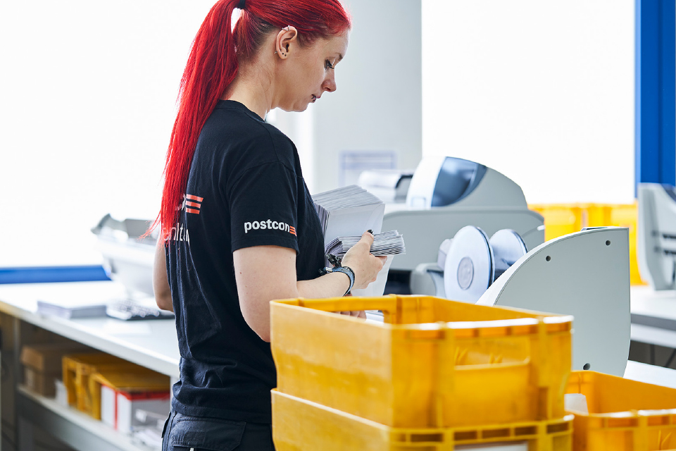 Postcon-Mitarbeiterin sortiert Briefe in gelbe Postkisten.