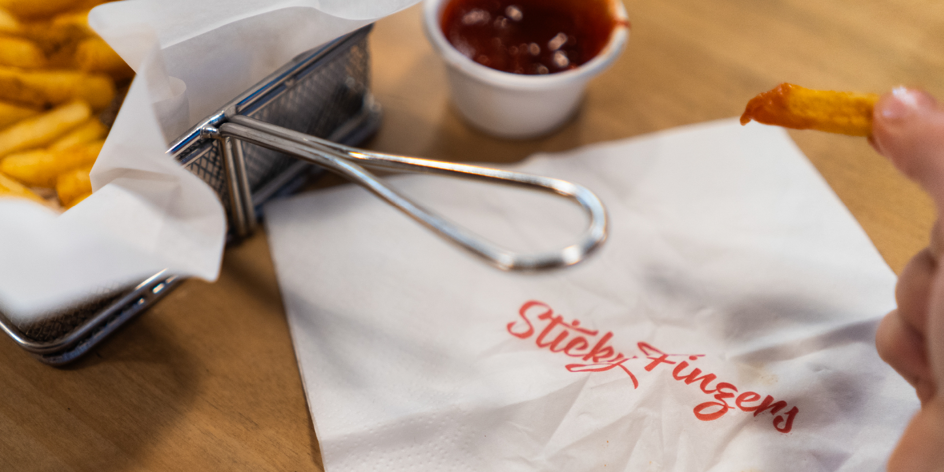 Pommes mit Ketchup in Metalkorb und Serviette mit Logo „Sticky Fingers“.