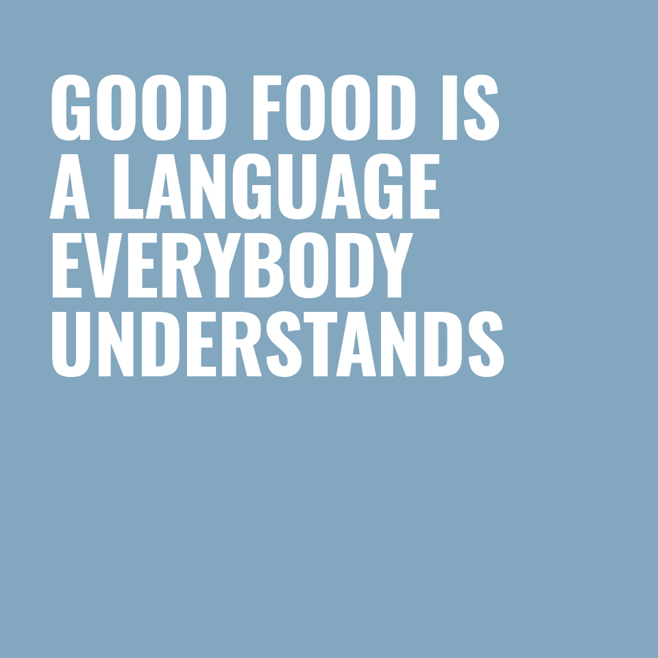 Weißer Schriftzug „GOOD FOOD IS A LANGUAGE EVERYBODY UNDERSTANDS“ auf hellblauem Hintergrund.