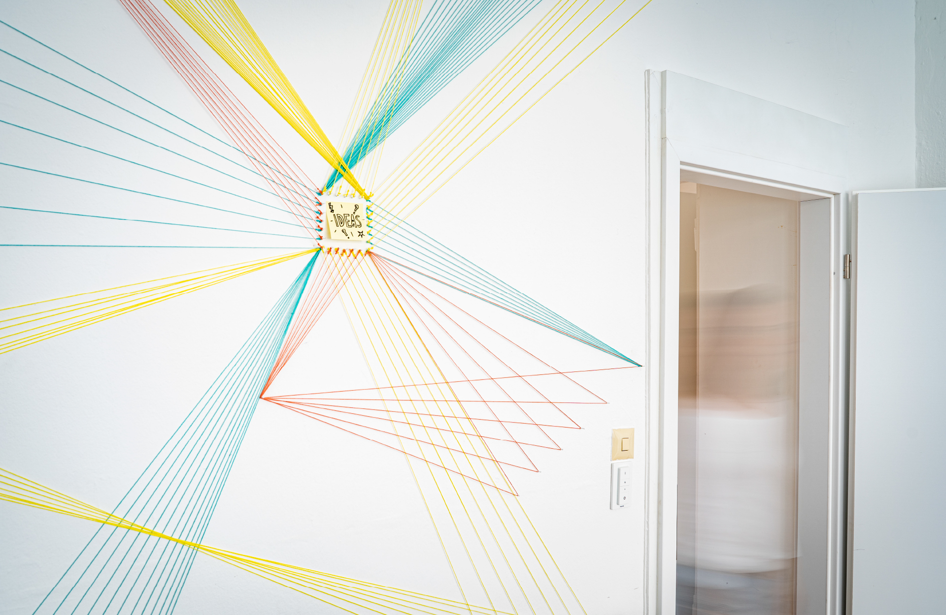 Rauminstallation aus bunten Fäden, die sich in einem Netzwerk über die ganze Wand spannen.