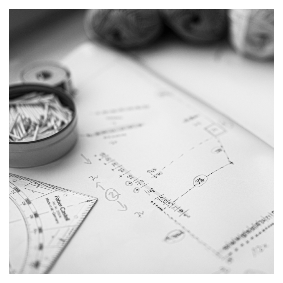 Schwarz-Weiß-Foto eines Arbeitsplans mit Skizzen und Maßen, daneben Nägel in einer Dose, Garnrollen und ein Geodreieck.