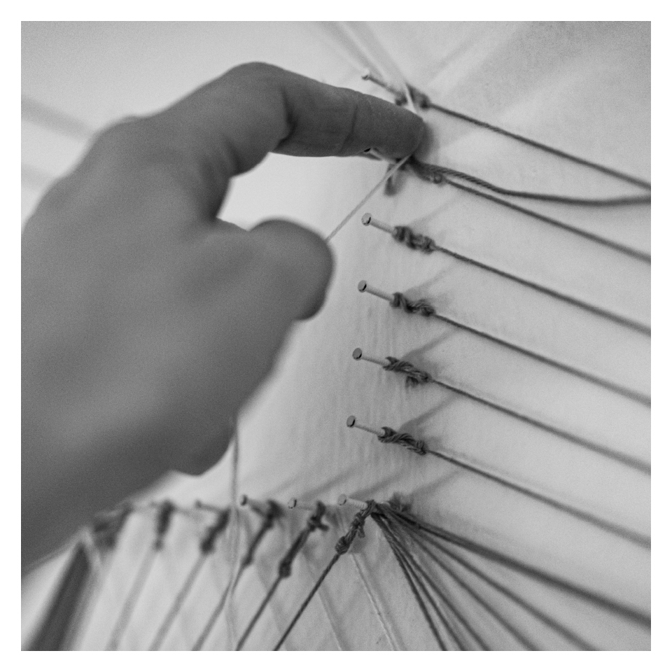 Schwarz-Weiß-Nahaufnahme einer Hand, die einen Faden an einem Nagel befestigt.